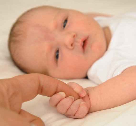 новорожденный  малыш держится  за  палец